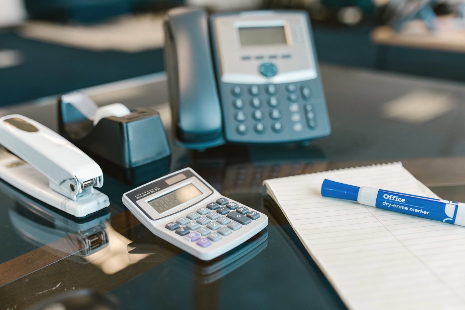 A desk telephone beside a notepad and calculator.
